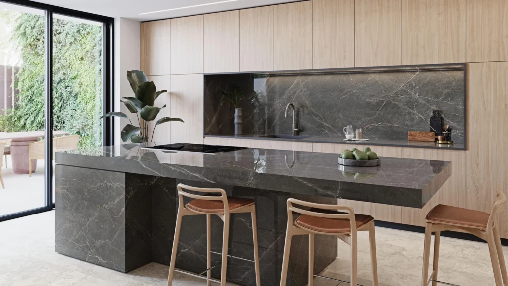 Luxury modern kitchen with a dark grey porcelain slab island and matching backsplash, light wood cabinetry, waterfall-edge countertop, built-in cooktop, bar stools, and large glass doors creating a bright, elegant space.
