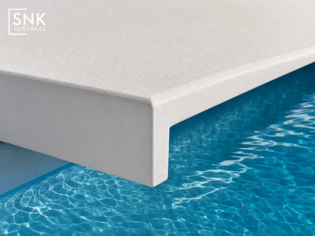 Extreme macro detail of drop-face porcelain pool coping showing the 90-degree profile edge over pool water.
